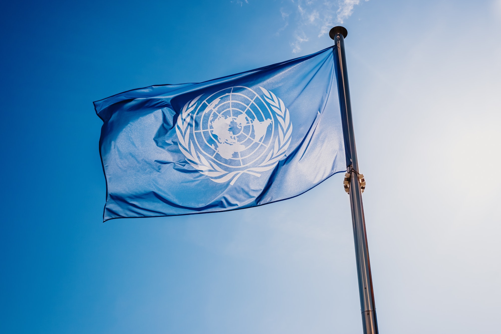 UN flag waved against the sun and blue sky.