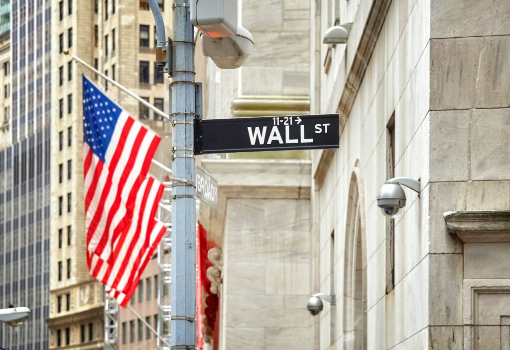 Wall Street sign with American flag in distance, NYC, USA.