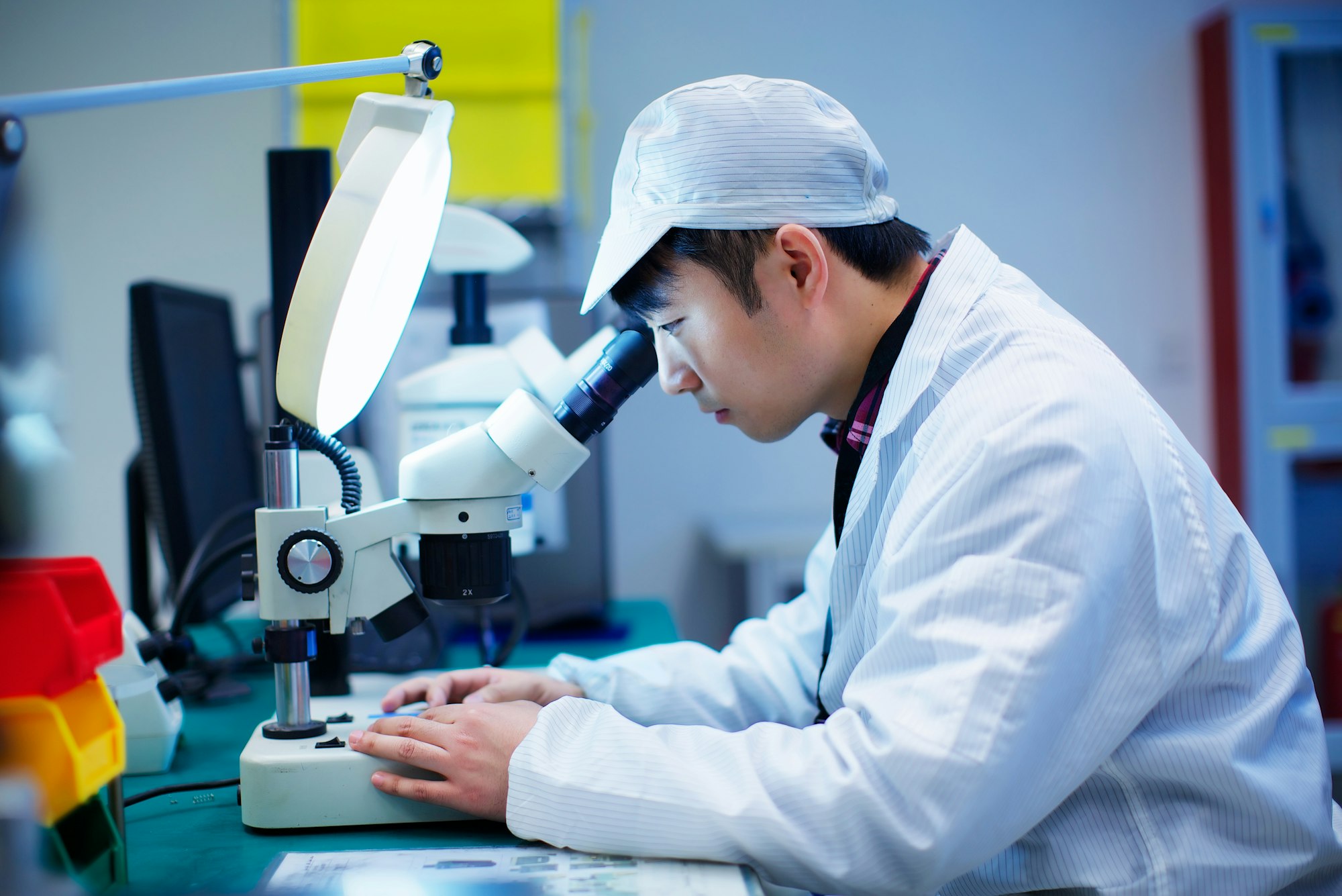 Workers at small parts manufacturing factory in China looking through microscope