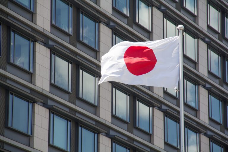 Low angle shot of the flag of Japan waving in the wind in front of the buildings on a sunny day