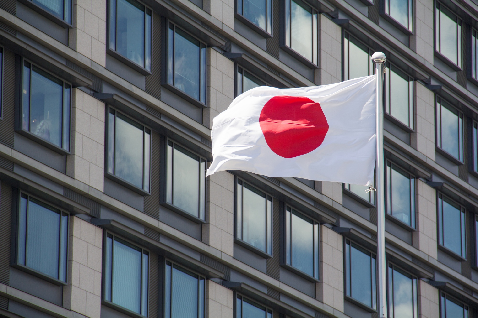 Low angle shot of the flag of Japan waving in the wind in front of the buildings on a sunny day