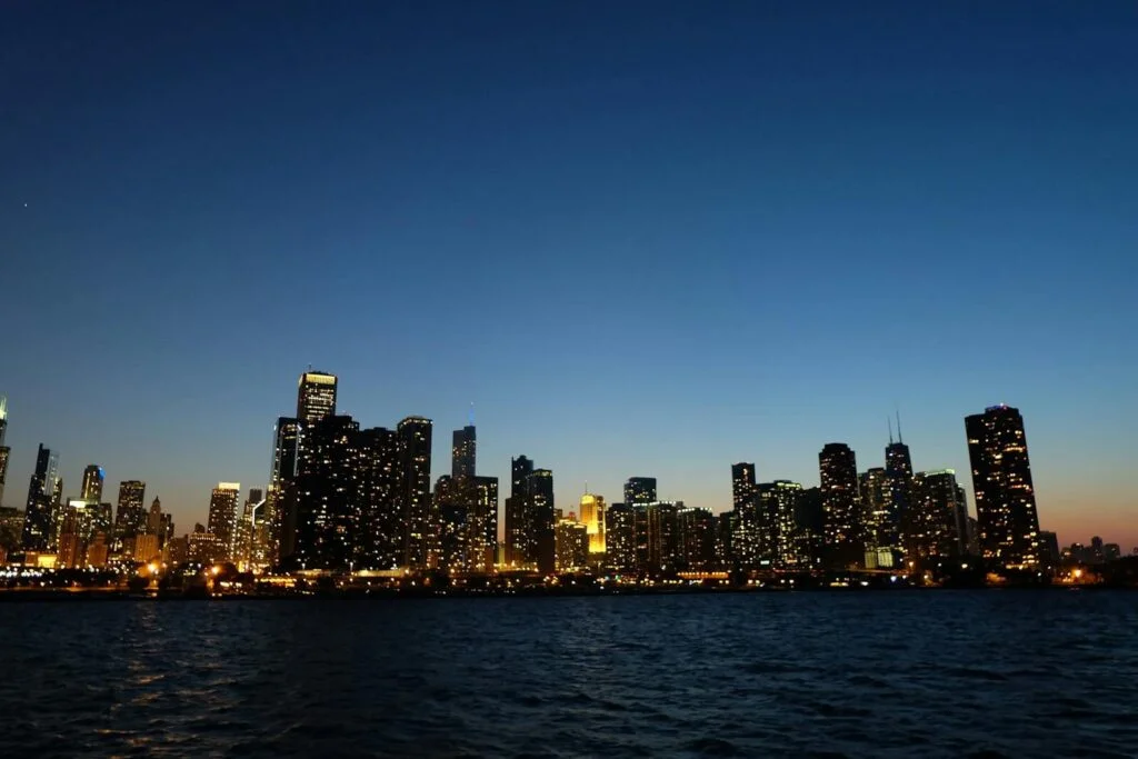 Capture of Chicago's skyline at dusk with illuminated skyscrapers reflecting on Lake Michigan.