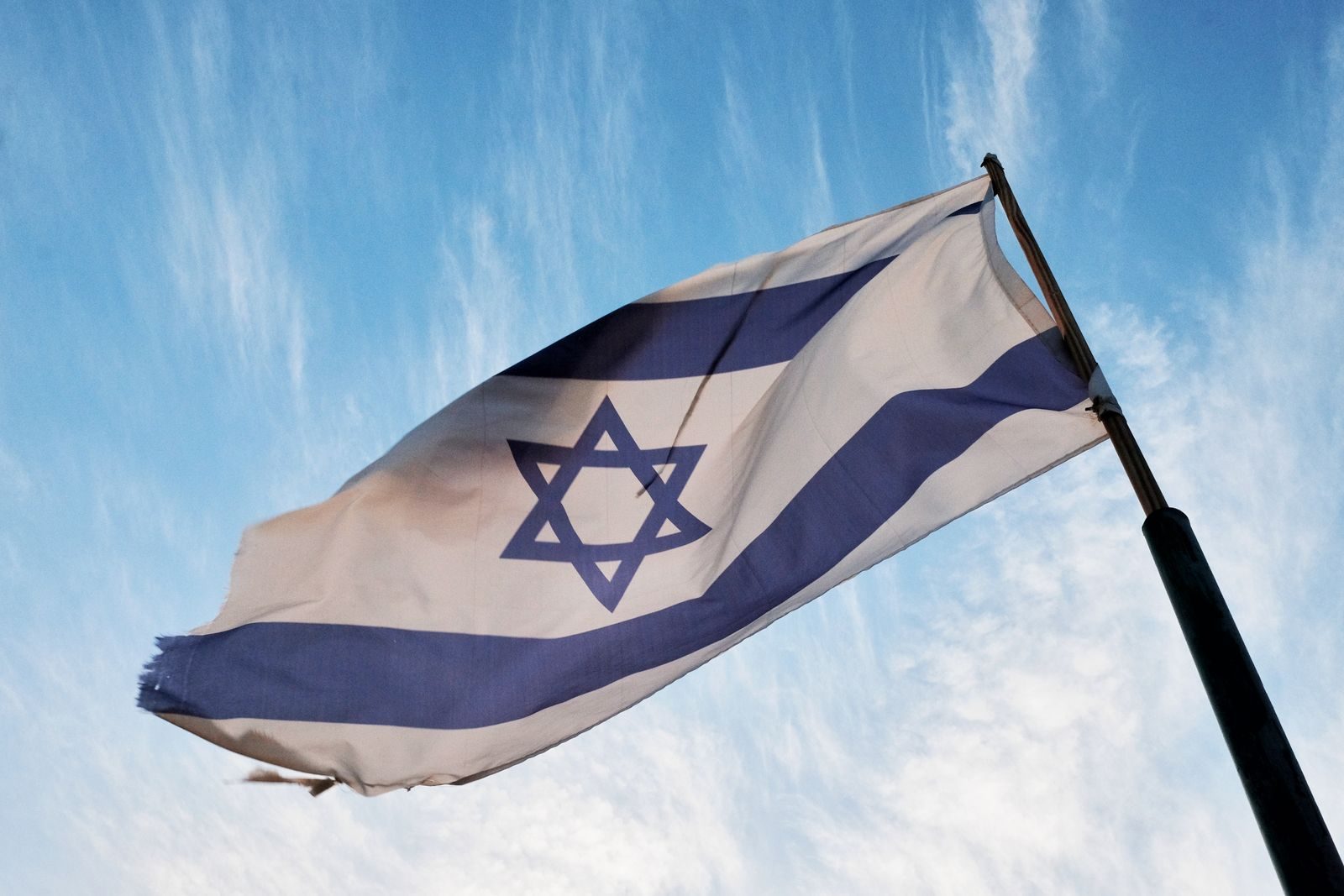 A close-up of the Israeli flag waving on a flagpole against a clear blue sky.