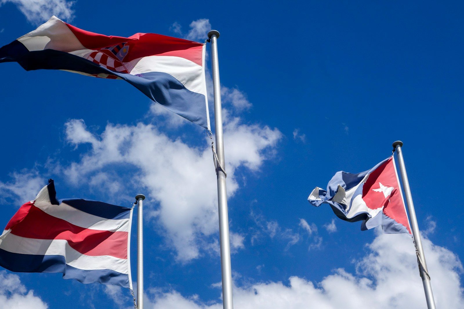 Three national flags waving against a blue sky